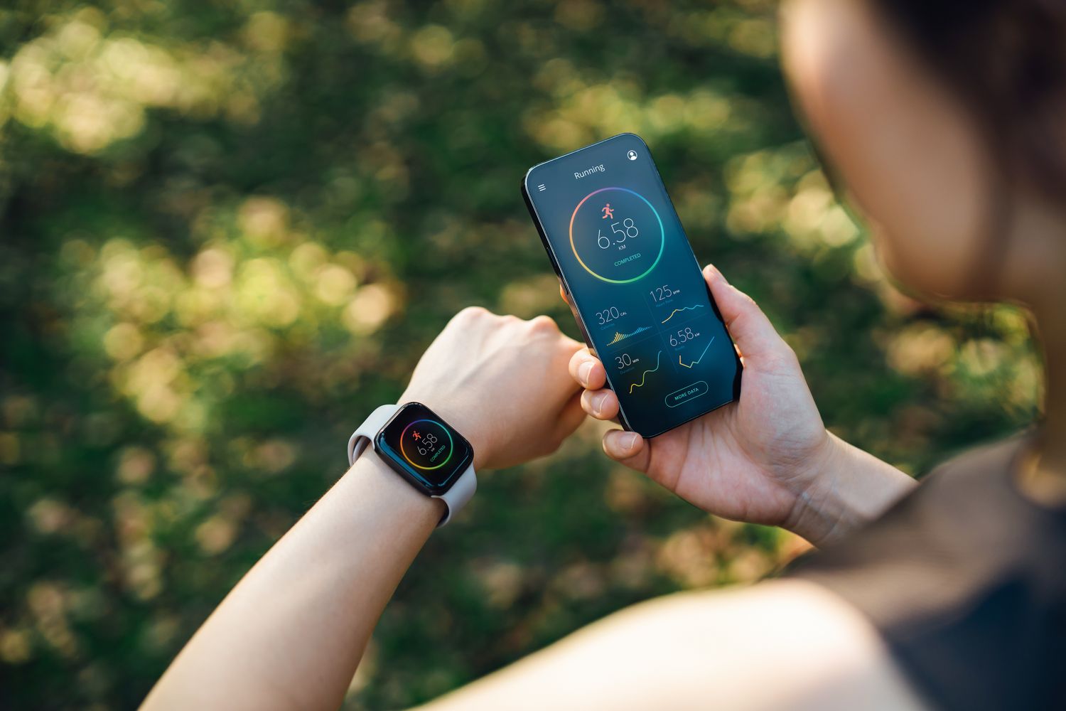 A woman outdoors looking at her wrist-based fitness tracker to check her health metrics.