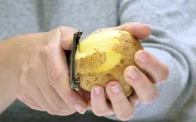 Close-up of a person peeling a raw potato for meal preparation.