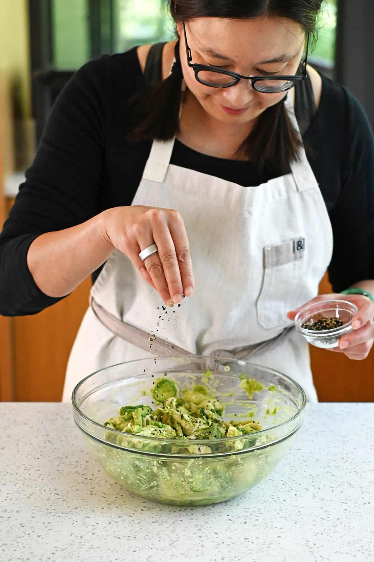 A woman sprinkling furikake seasoning over a bowl of avocado chicken salad.