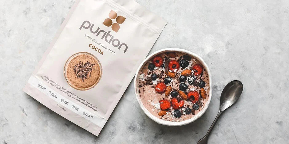 A wooden bowl filled with a dairy-free breakfast cereal or smoothie bowl topped with nuts and cocoa powder.