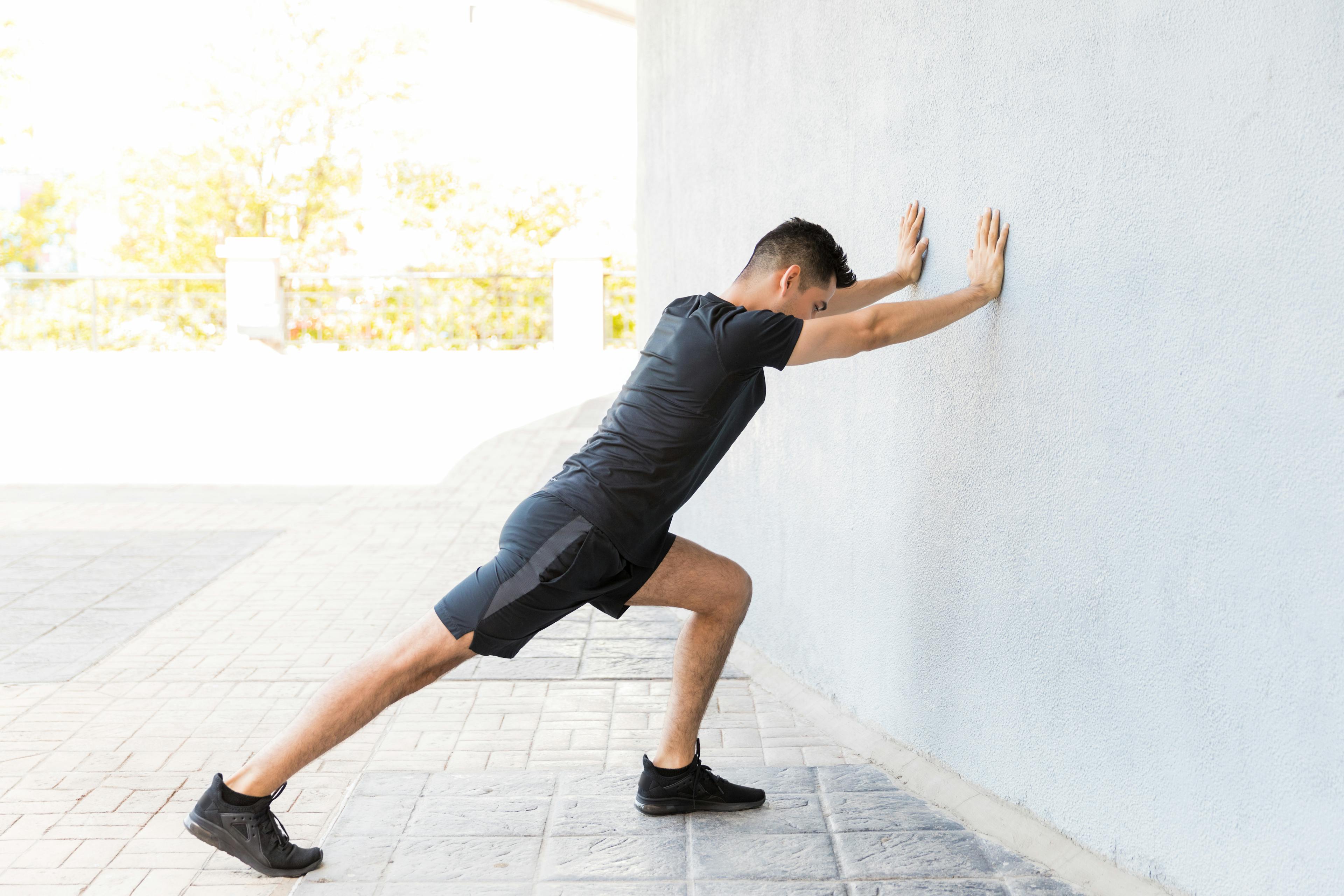 A person performing a wall-assisted calf stretch with one leg extended back.