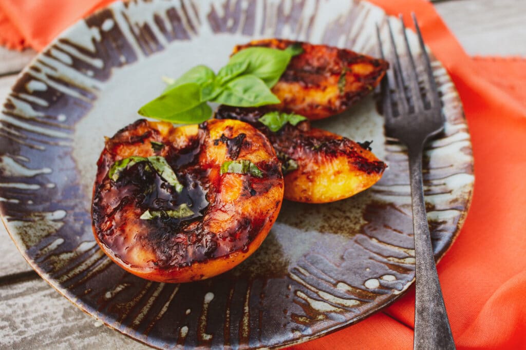 Halved peaches with char marks from a grill on a serving plate.