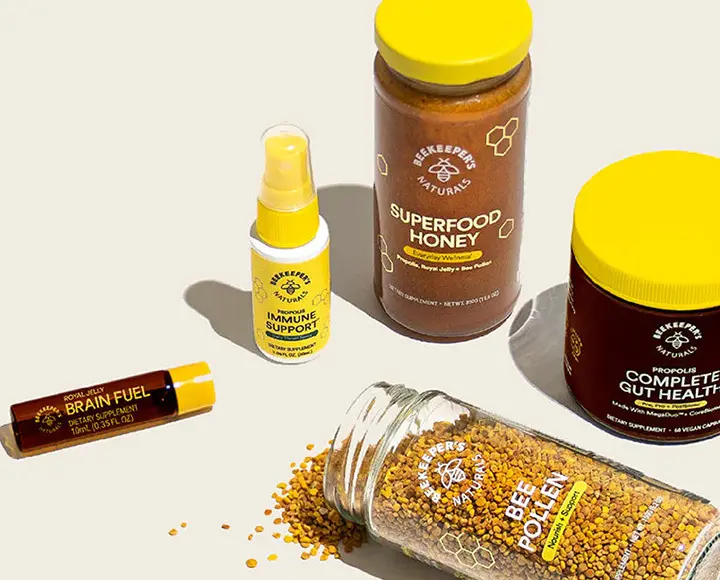 Bottles of propolis throat spray and jars of bee pollen pellets on a clean surface.