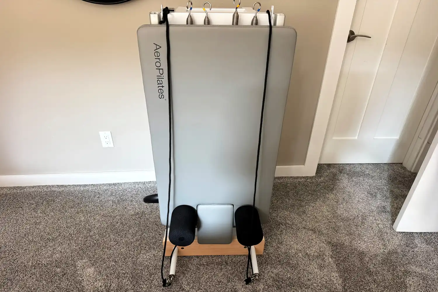 An AeroPilates reformer folded vertically and standing against a wall in a room.
