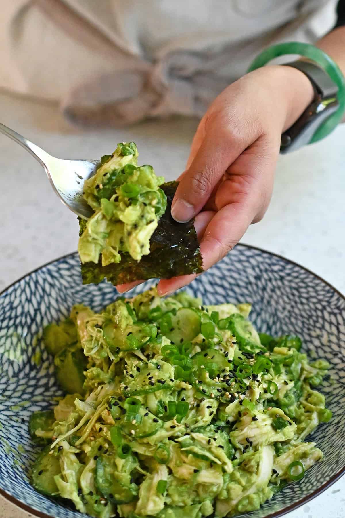 A spoonful of avocado chicken salad being placed onto a sheet of toasted seaweed.