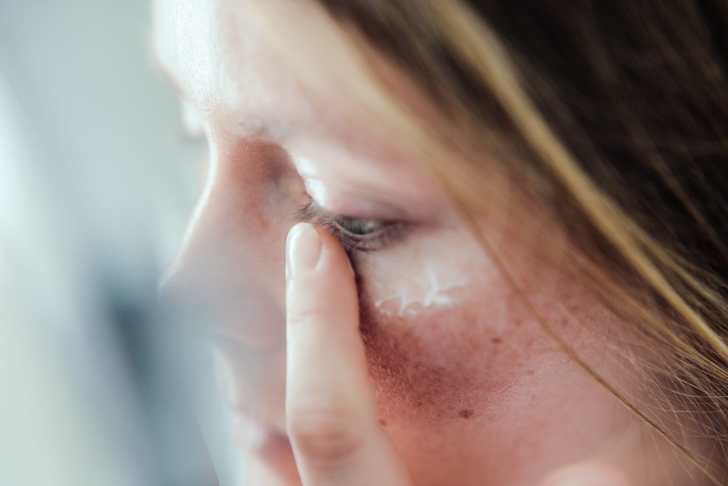 Close-up of a woman with clear skin applying face cream.