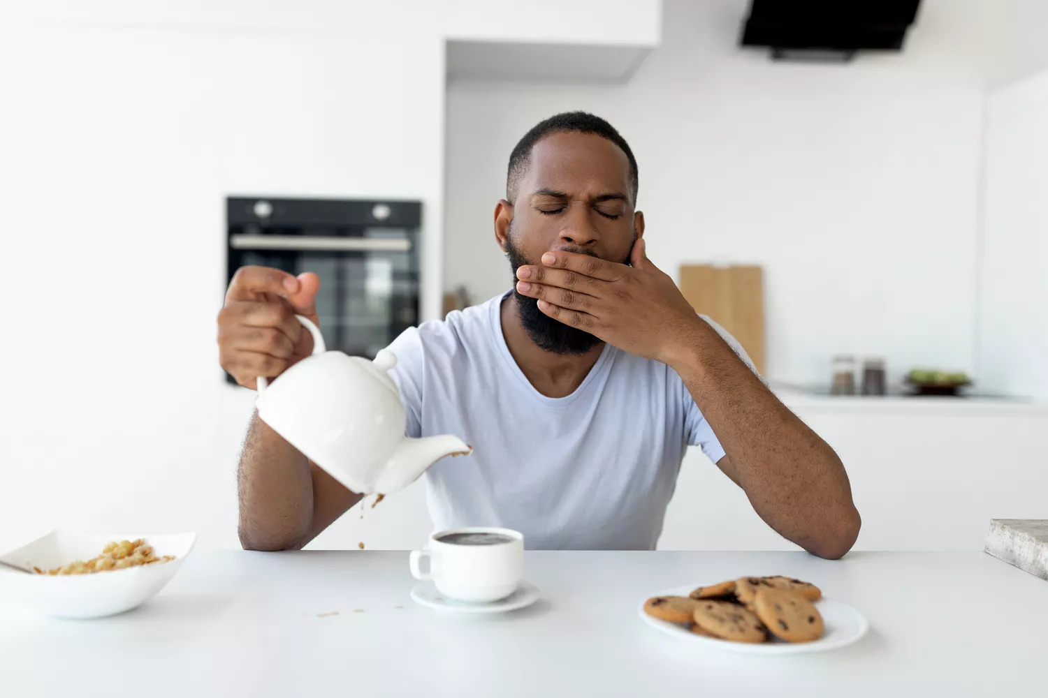 A tired man yawning while pouring a cup of coffee.