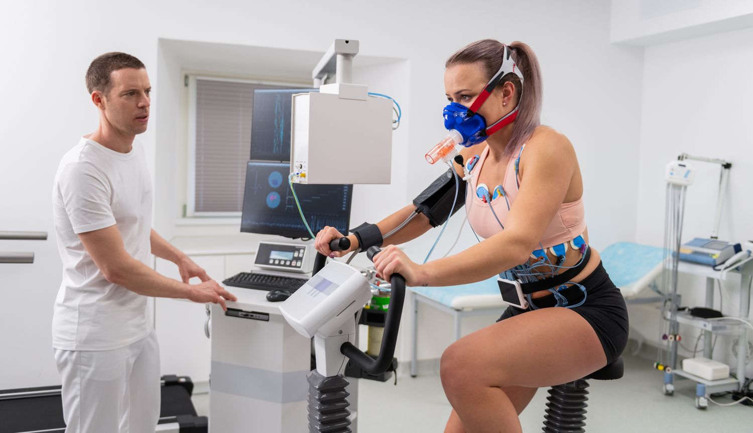 A woman performing a stress test on a stationary bike while connected to cardiac monitoring equipment.
