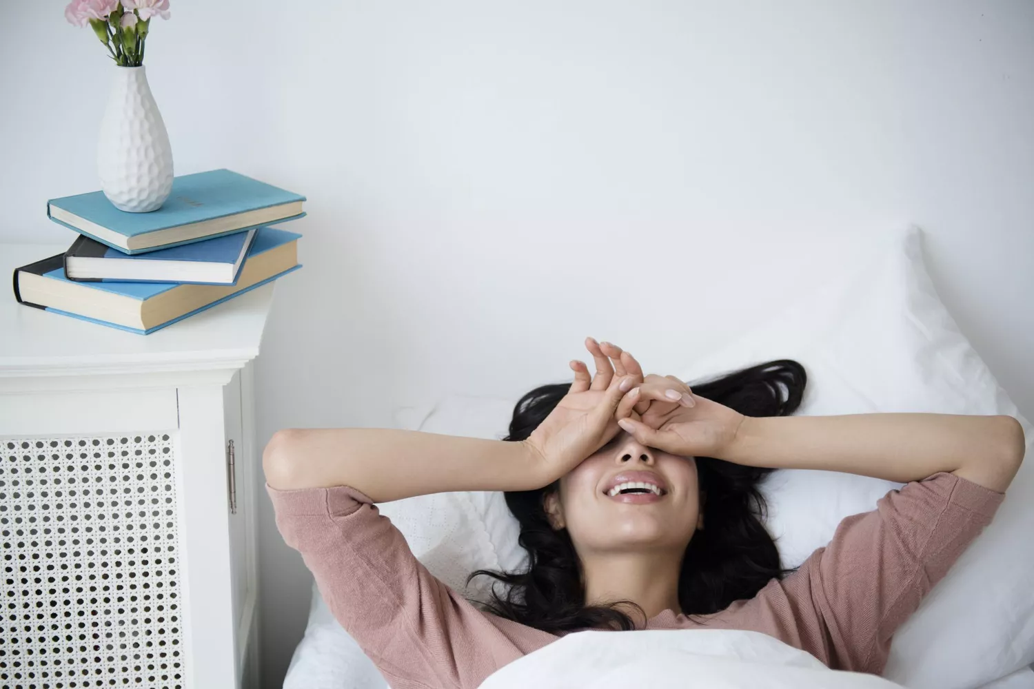 A person sitting up in bed looking exhausted and rubbing their eyes.